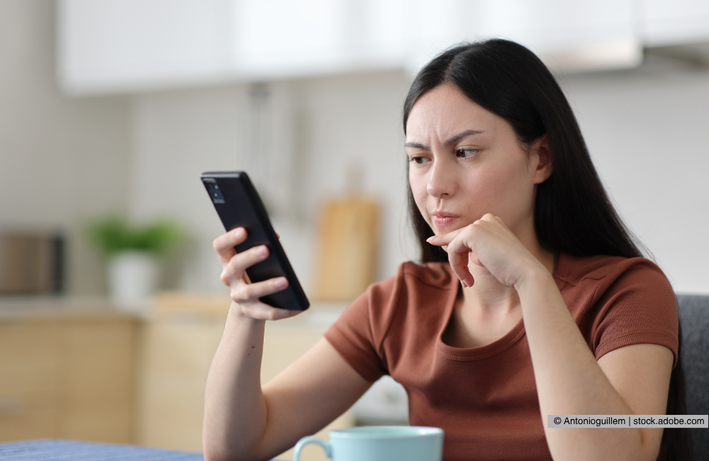 Eine Frau schaut sich ihr Handy an und schaut dabei nachdenklich. 
