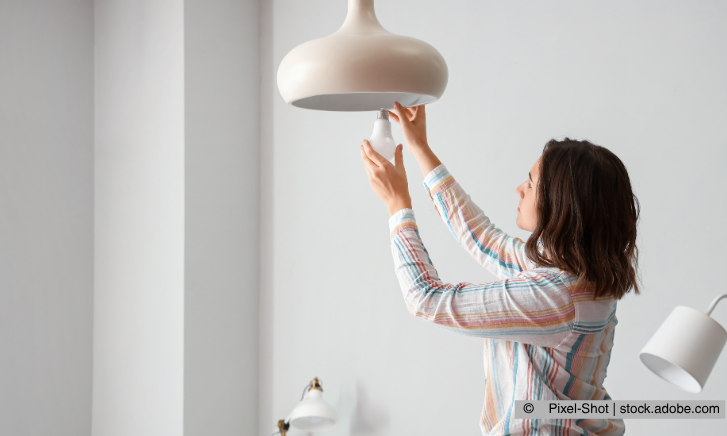 Frau schraubt neue Birne in Deckenlampe