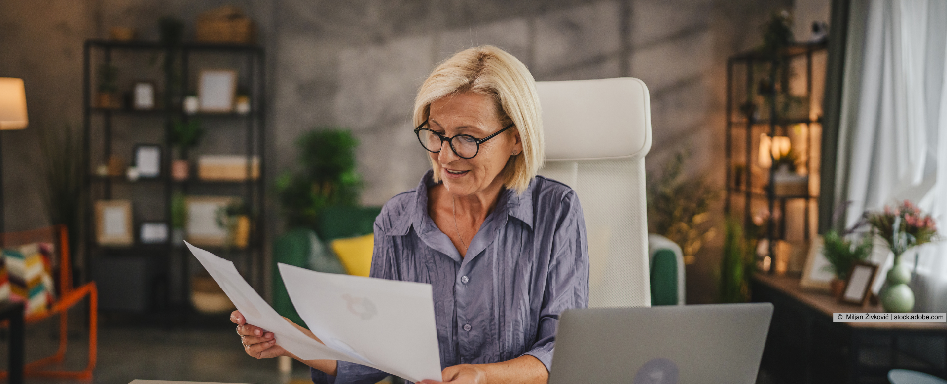 Eine Frau blättert am Schreibtisch vor ihrem Laptop