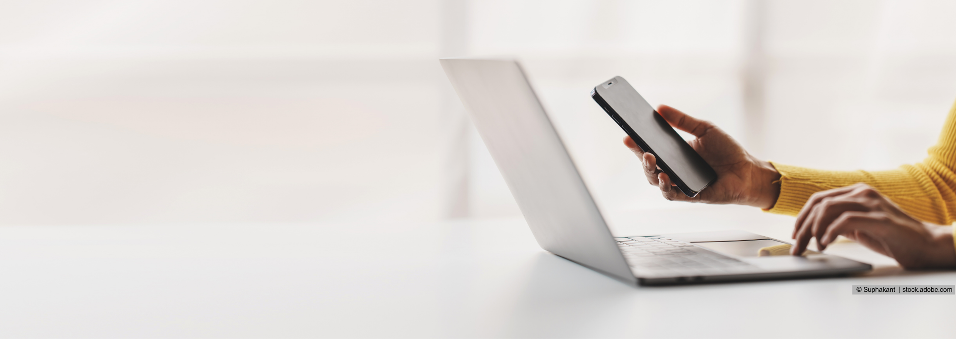 Person sitzt vor Laptop und benutzt währenddessen ein Handy