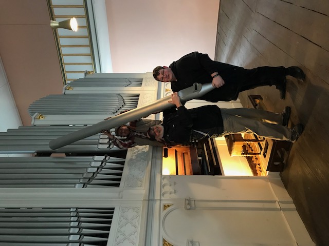 Herr Kutter Junior( oben )  Herr Schneider ( links)und der Organist Herr Anschütz(rechts) halten eine Orgelpfeife vor der Orgel stehend