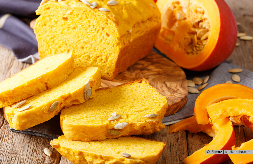 Kürbisbrot auf einem Brettchen im Hintergrund ist ein Kürbis zu sehen