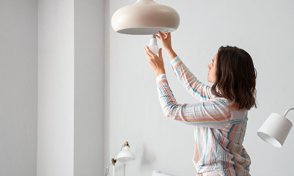 Frau schraubt neue Birne in Deckenlampe