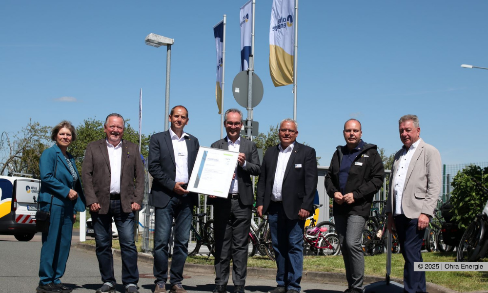 Die Übergabe des Zertifikates erfolgte zu Familienfest der Ohra Energie. Im Hintergrund sind die wehenden Fahnen zu sehen während Dr. Florian Reißmann und Volkmar Braune das Zertifikat in den Händen halten. v.l.: Sylke Niebur (Erste Beigeordnete Landratsamt Gotha), Klaus Reißig (Vorsitzender Aufsichtsrat Ohra Energie GmbH), Volkmar Braune (Technischer Leiter und Prokurist Ohra Energie GmbH), Dr. Florian Reißmann (Geschäftsführer der DVGW-Landesgruppe Mitteldeutschland), Michael Fischer (Geschäftsführer Ohra Energie GmbH), Mario Stötzer (Leiter Netzbetrieb Ohra Enegrie GmbH), Uwe Oßwald (Geschäftsführer der Kommunalbeteiligung Ohra Energie GmbH) bei der Übergabe des TSM-Zertifikats. Foto: Christiane Specht