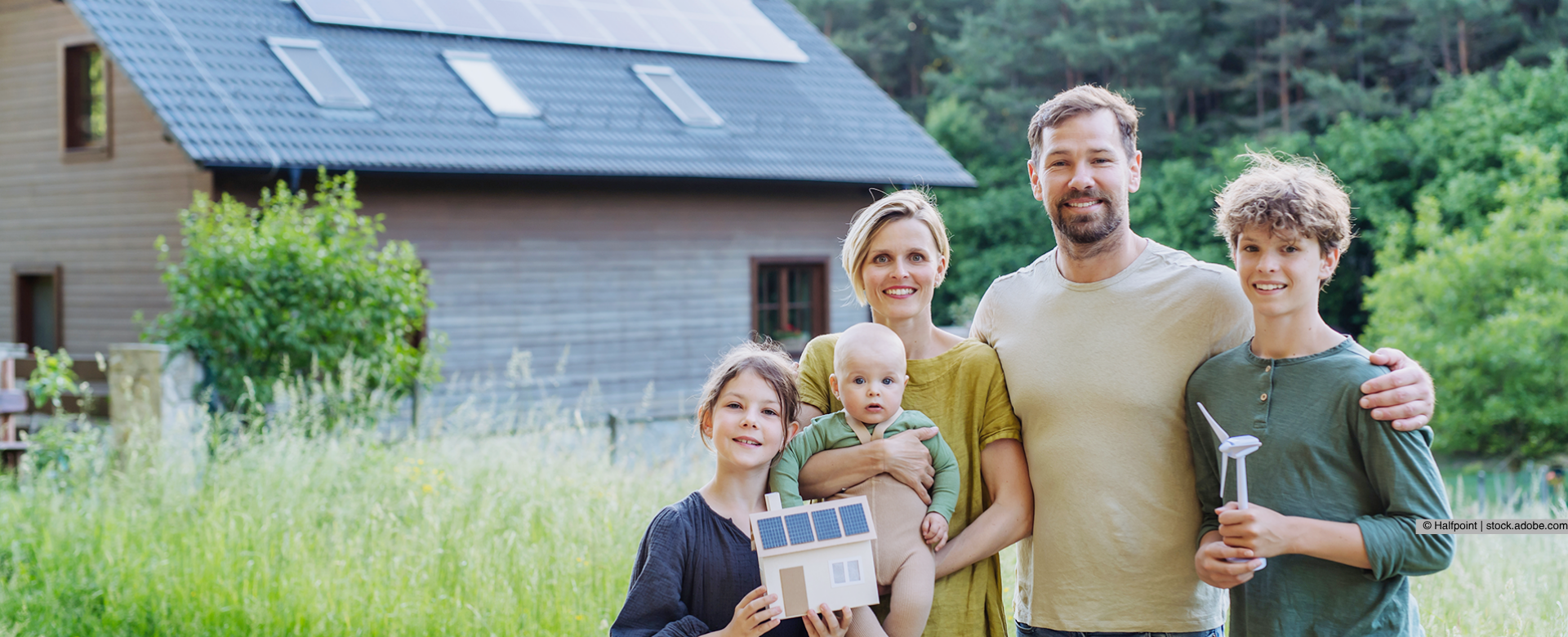 Eine Familie steht vor einem Haus in einer Wiese