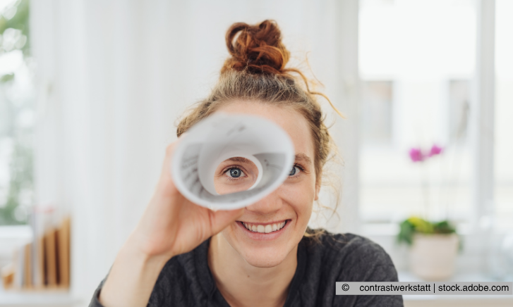 Frau schaut lächelnd durch ein gerollltes Blatt 