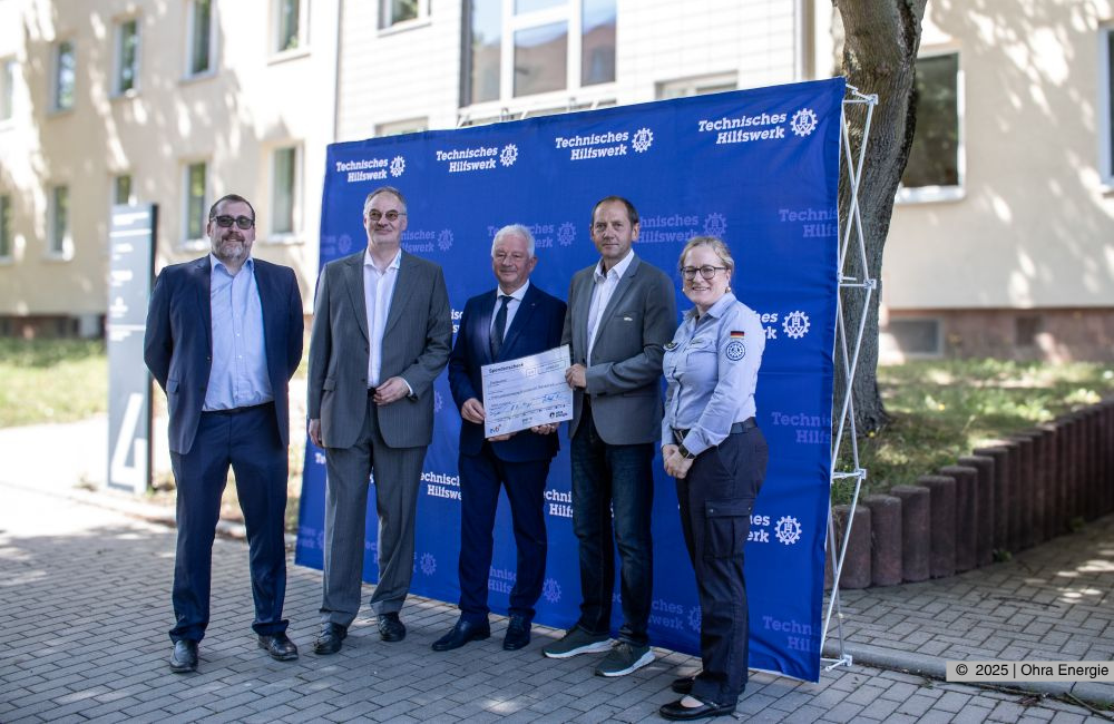 Die Beiteiligten bei der Spendenübergabe v.l. Lisa Dittrich (Bereichsleiterin vom Sonnenhof), Jörg Schlothauer (Bürgermeister Wutha-Farnroda), Anne-Juliane Pogander (Geschäftsführerin Diakonie GmbH), Michael Fischer (Geschäftsführer Ohra Energie GmbH), Lisa Sophie Große (Erzieherin), Silvana Zink (Marketing/Vertrieb Ohra Energie GmbH). Dabei stehen sie vor einer Leinwand und dem Gebäude des THW. Fotografin: Christiane Specht